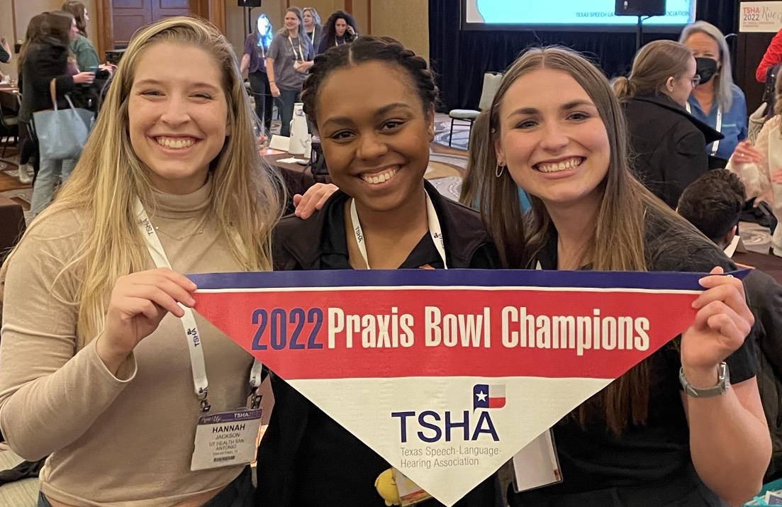 Three students smiling and holding a small championship banner