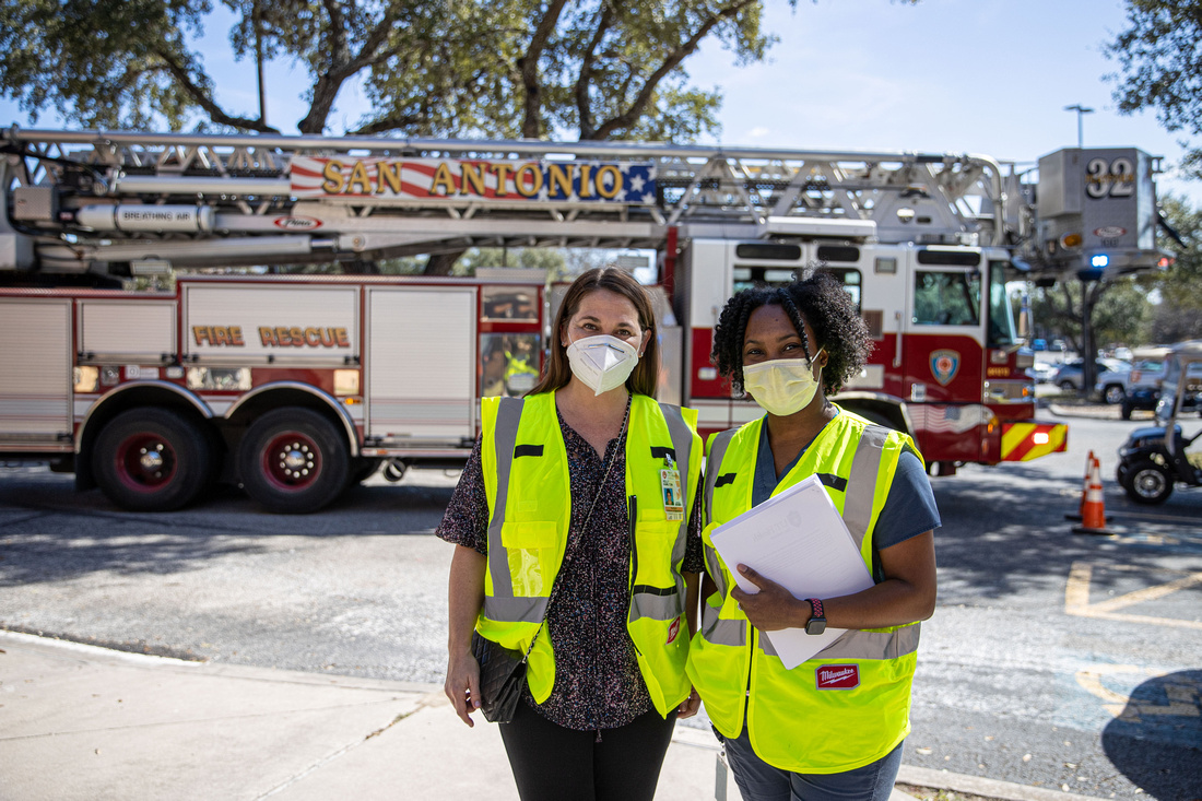 two public health workers standing in front of a fire truck wearing high visibility vests.