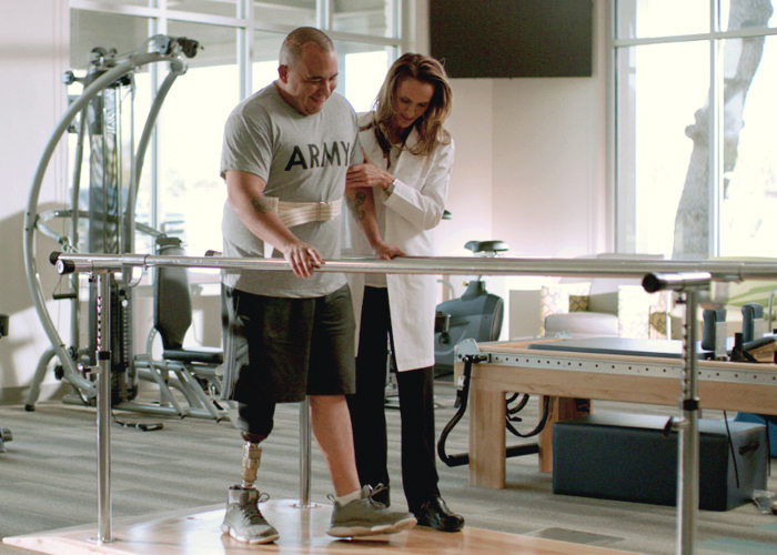 amputee patient with prosthetic leg being rehabilitated with aid of therapist